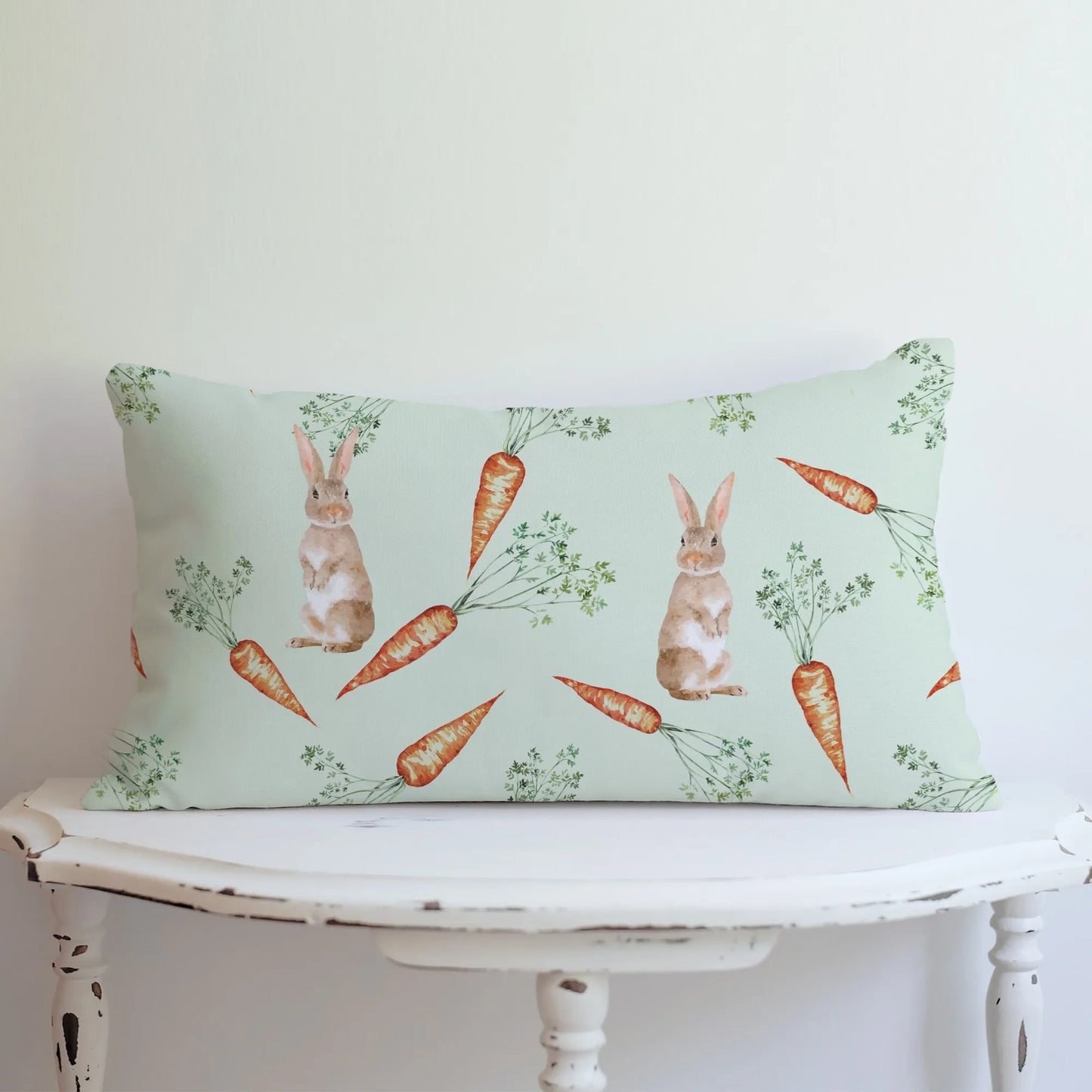 Light green lumbar pillow with a watercolor bunny and carrot pattern displayed on a white table, ideal for subtle spring decor.