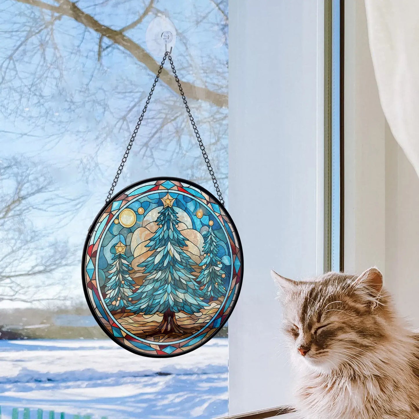 Christmas tree stained glass ornament hanging by a window, casting shimmering blue tones in a winter setting.