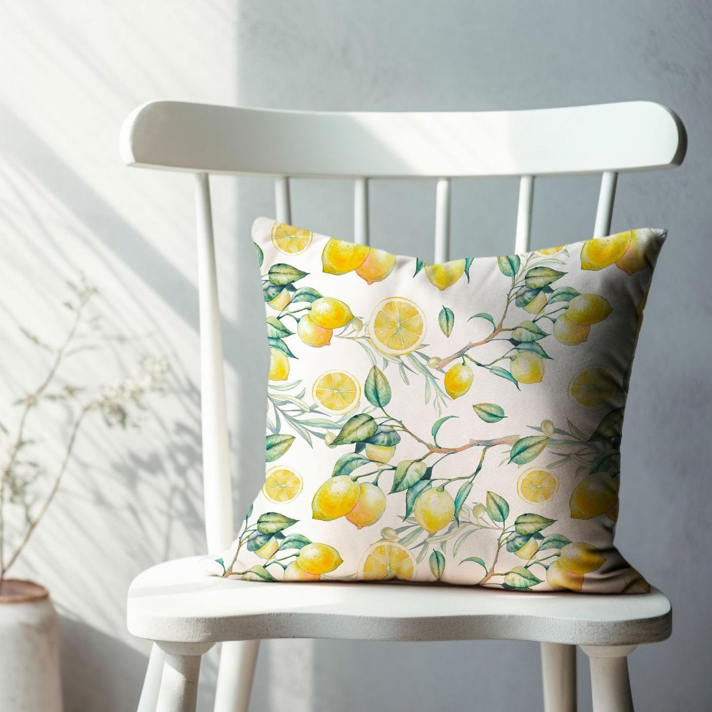 White pillow with yellow lemons and green leaves on a white chair – fresh summer decor.