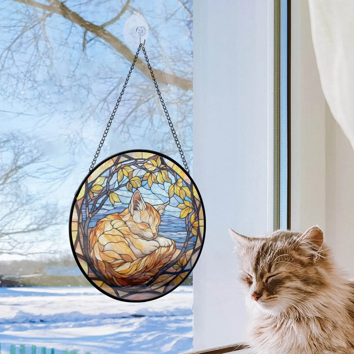 Stained glass cat ornament hanging in window with real cat resting nearby on snowy day