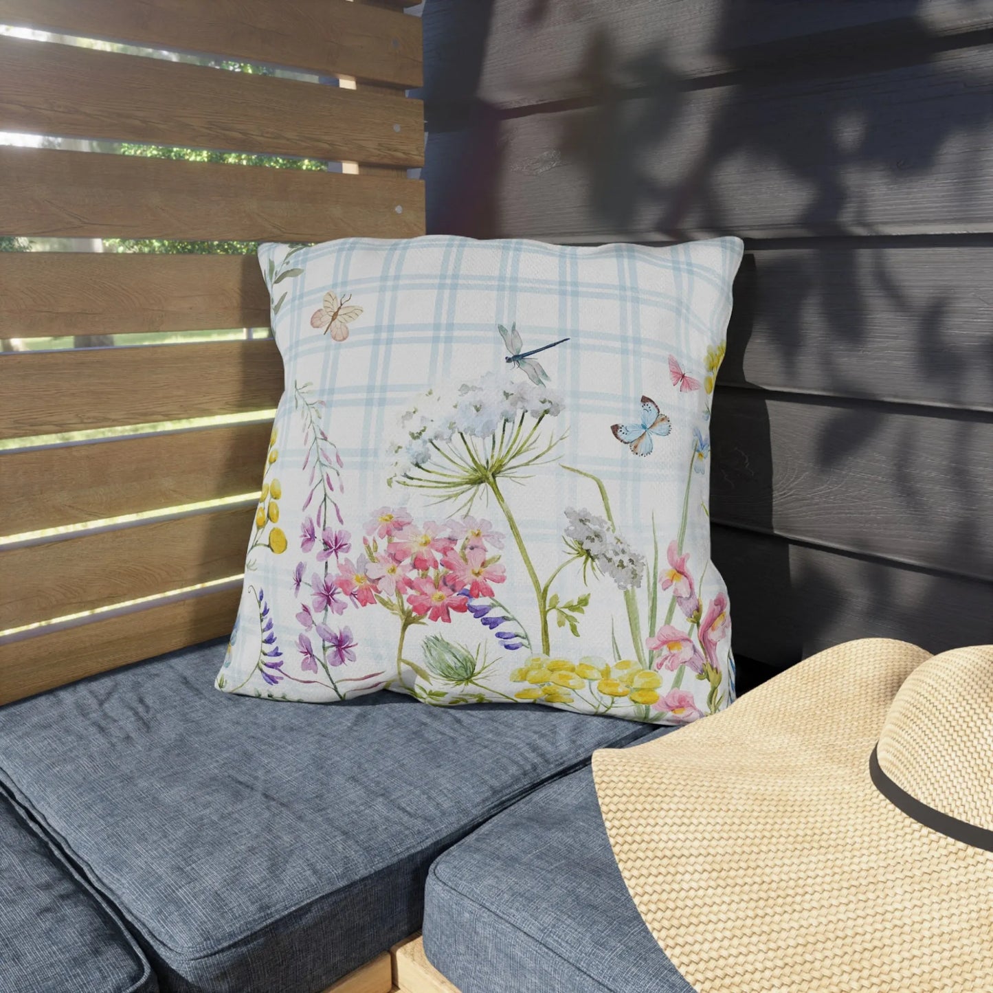 Nature-inspired outdoor pillow with watercolor wildflowers and butterflies on blue gingham, styled on patio bench for spring garden vibes.