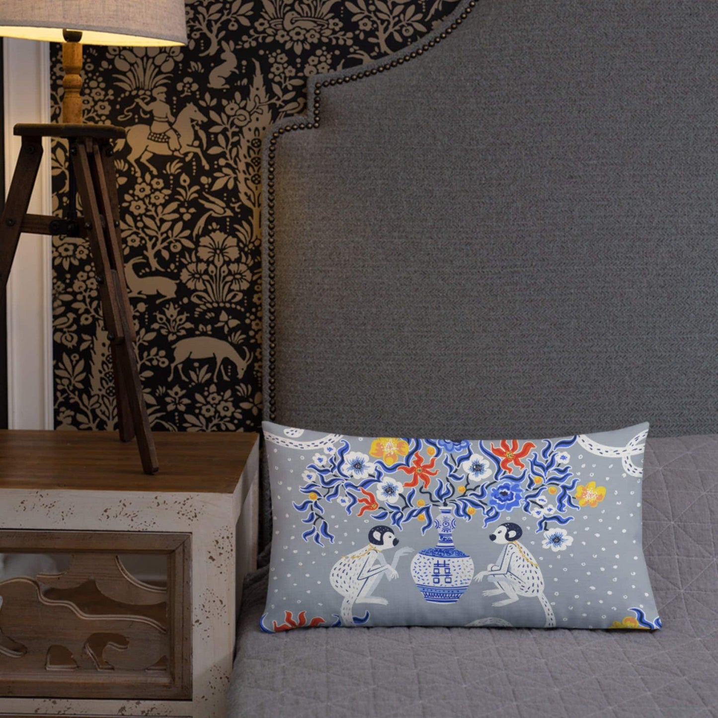 Chinoiserie monkey lumbar pillow on bed. Oriental design with blue pagoda vase and floral accents.