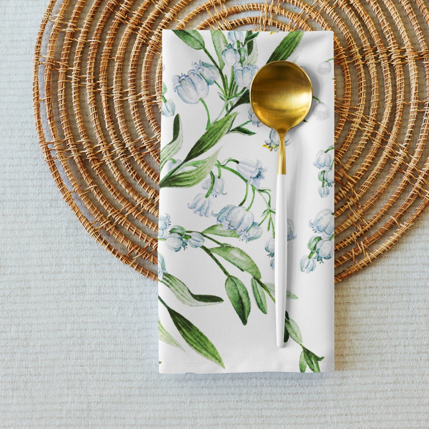 Lily of the Valley table setting with a floral napkin and gold spoon on a woven placemat.