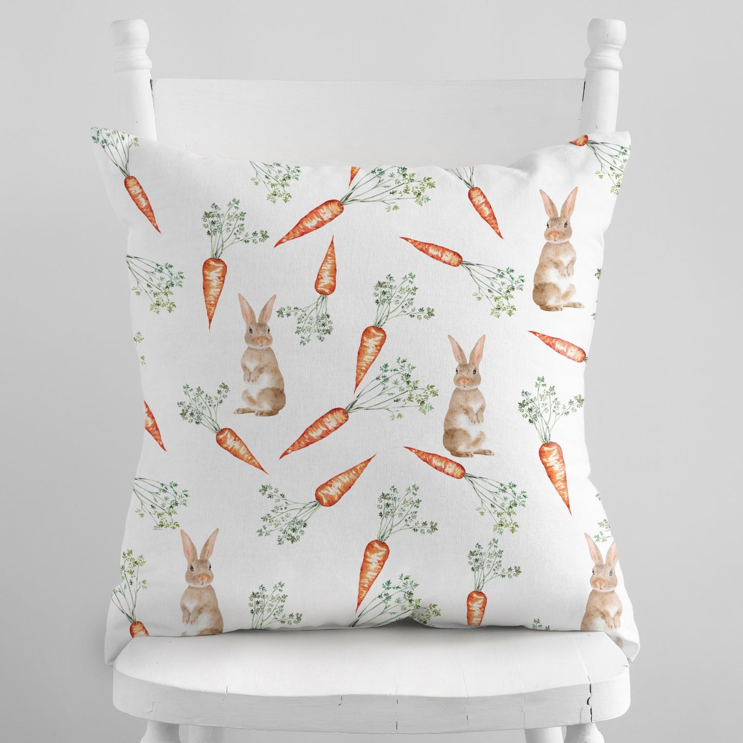 White throw pillow with a watercolor pattern of bunnies and carrots, perfect for spring and Easter decor.
