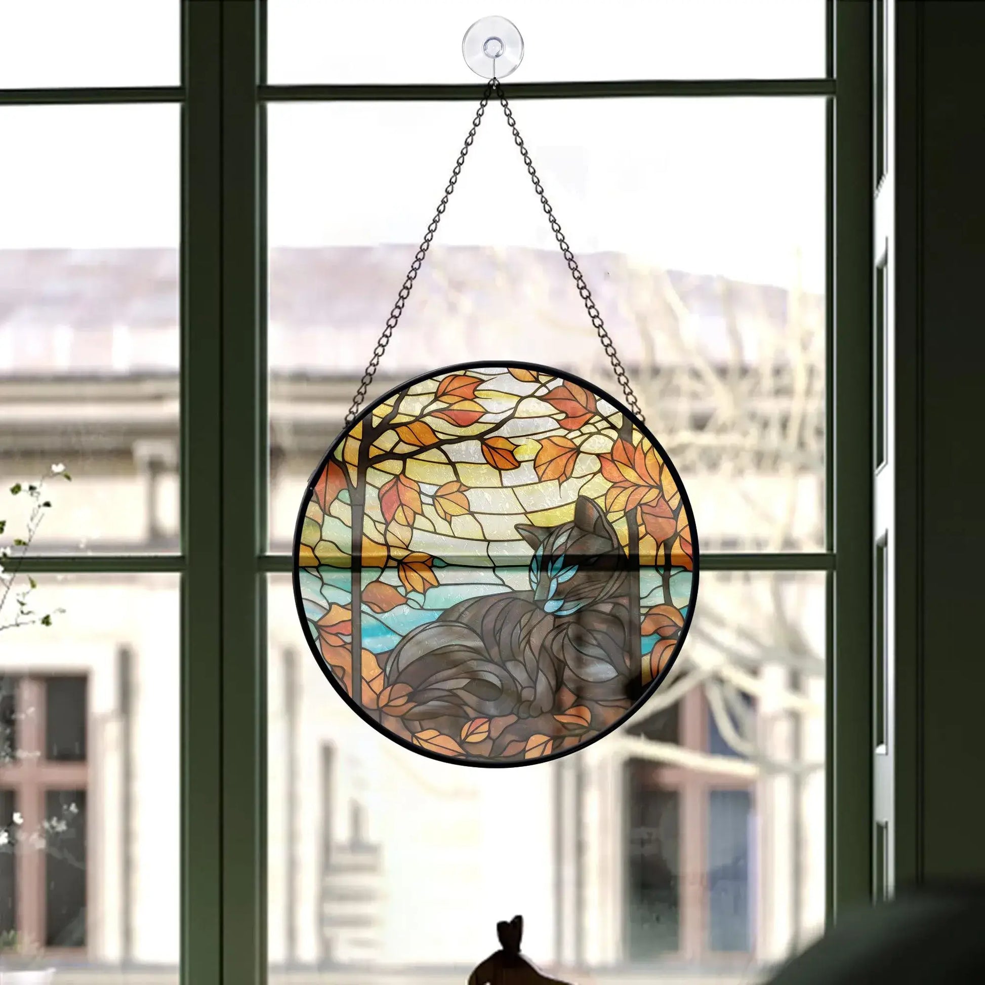 Black cat stained glass ornament with fall leaves, hanging in a sunlit window