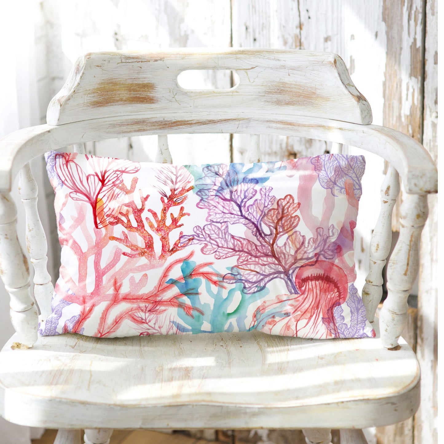 Coral reef lumbar pillow on white rustic chair. Ocean-themed decorative pillow with coral and jellyfish design.