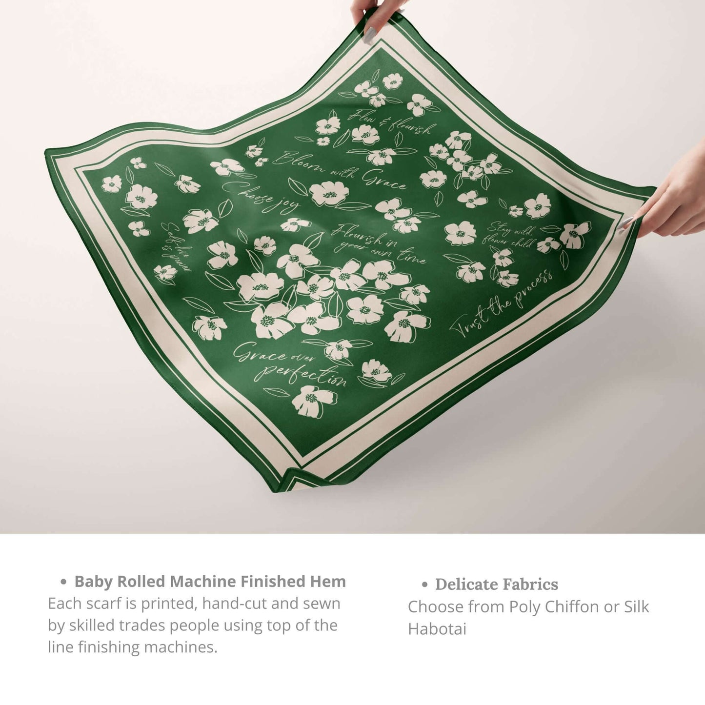 Hands holding an emerald green silk scarf with white wildflower and affirmation design, showcasing the hem and fabric options.