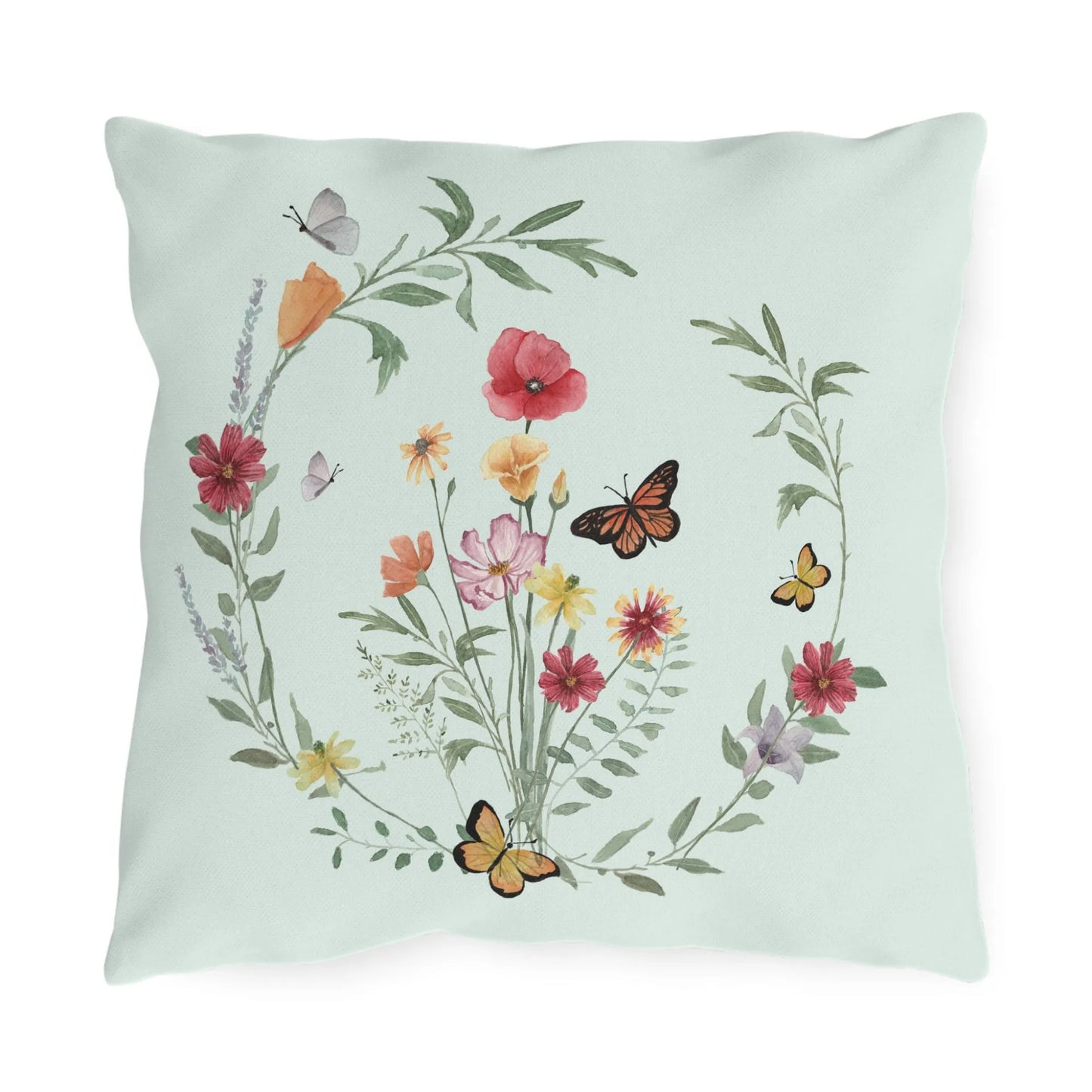 Nature-inspired outdoor pillow with watercolor wildflowers and butterflies in a circular wreath design on soft sage green background.