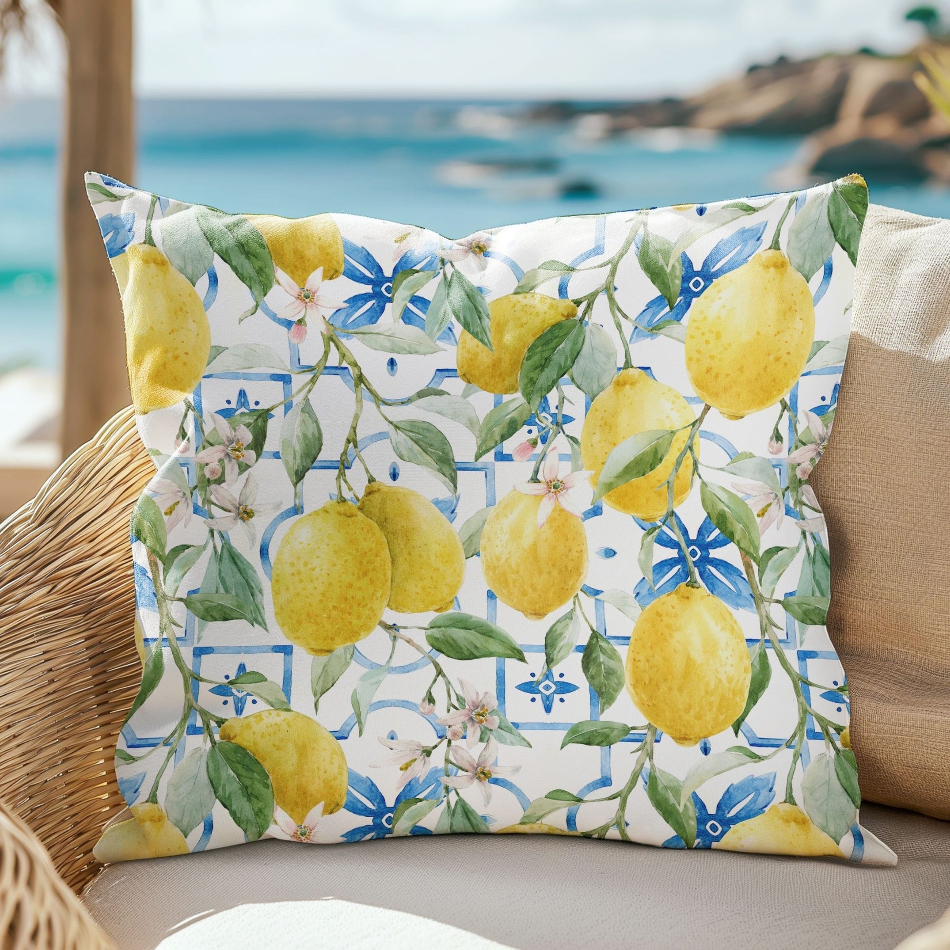 Watercolor Italy Lemon Outdoor Pillow sitting on rattan chair with beach behind