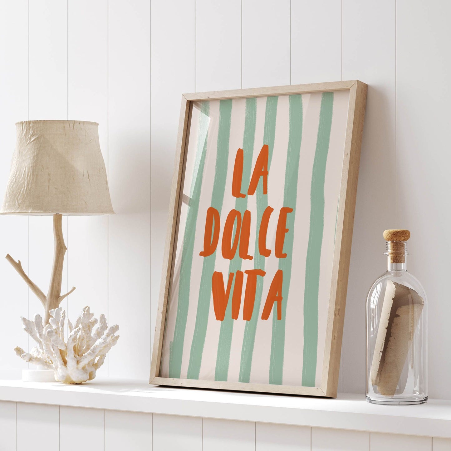 La Dolce Vita print with mint green stripes and orange text, styled on a shelf with driftwood lamp and glass bottle decor