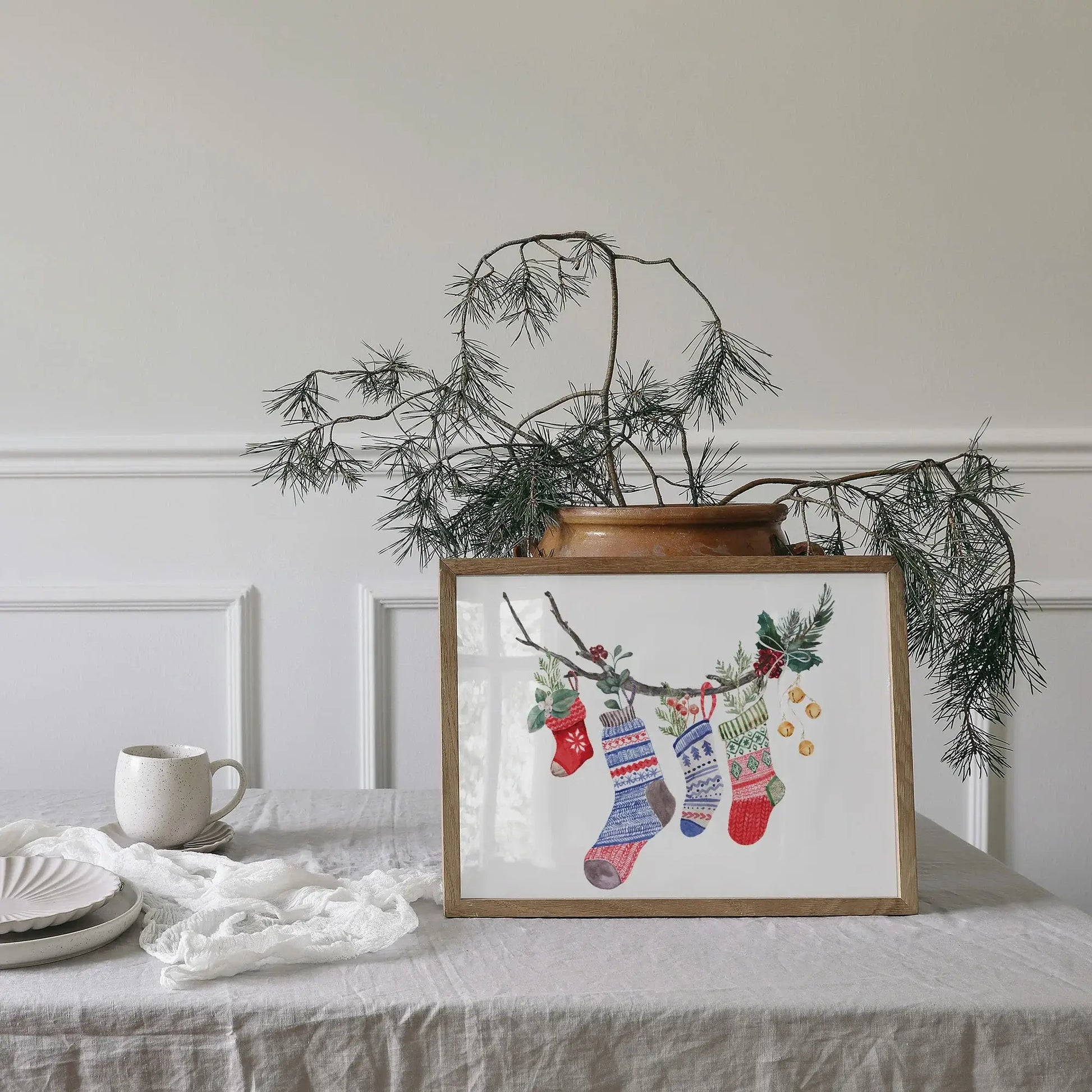 Watercolor Christmas Stocking Art Print displayed in a wooden frame with holiday decorations and cozy setting.