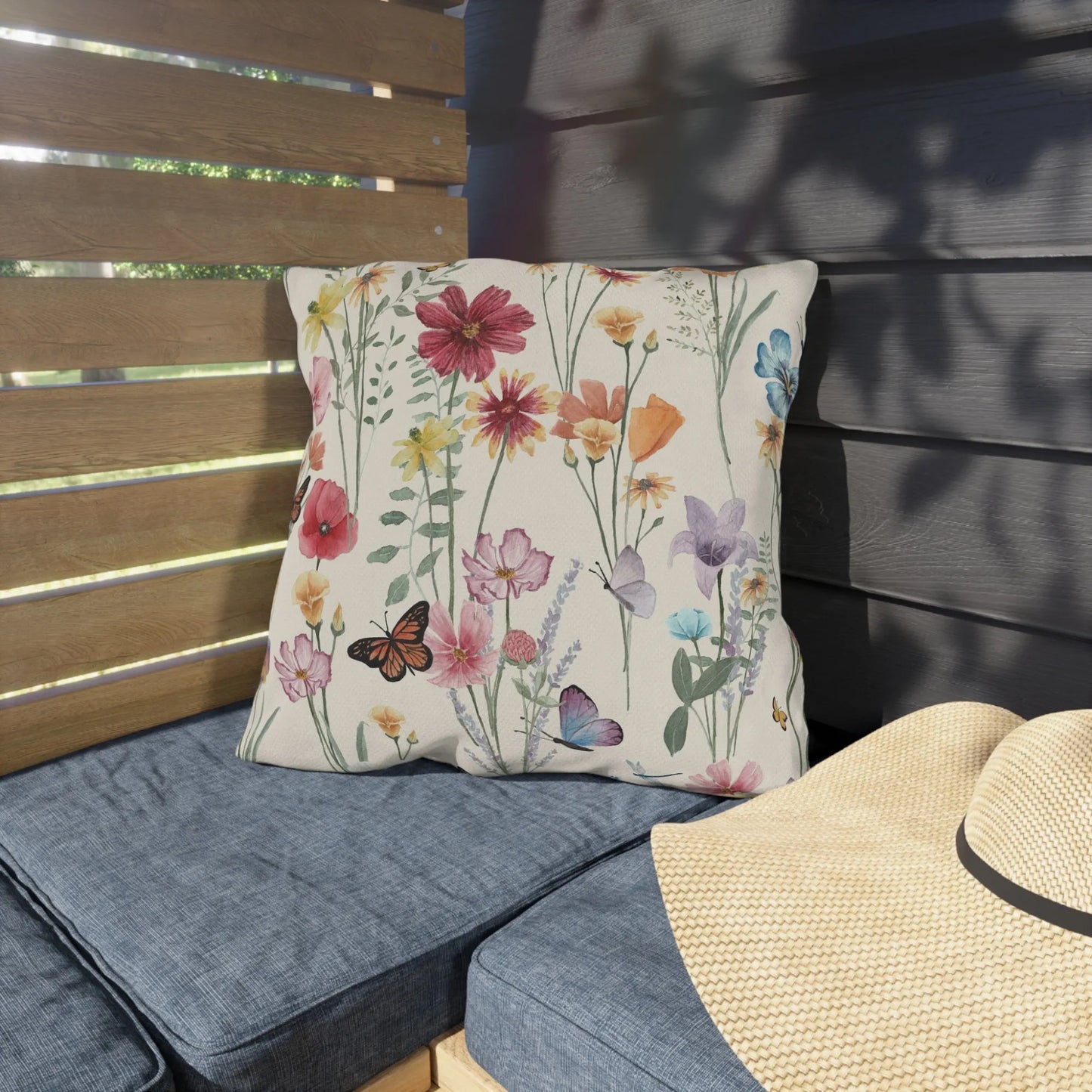 Watercolor wildflower outdoor pillow on patio bench with blue cushions, perfect for garden or balcony seating décor.