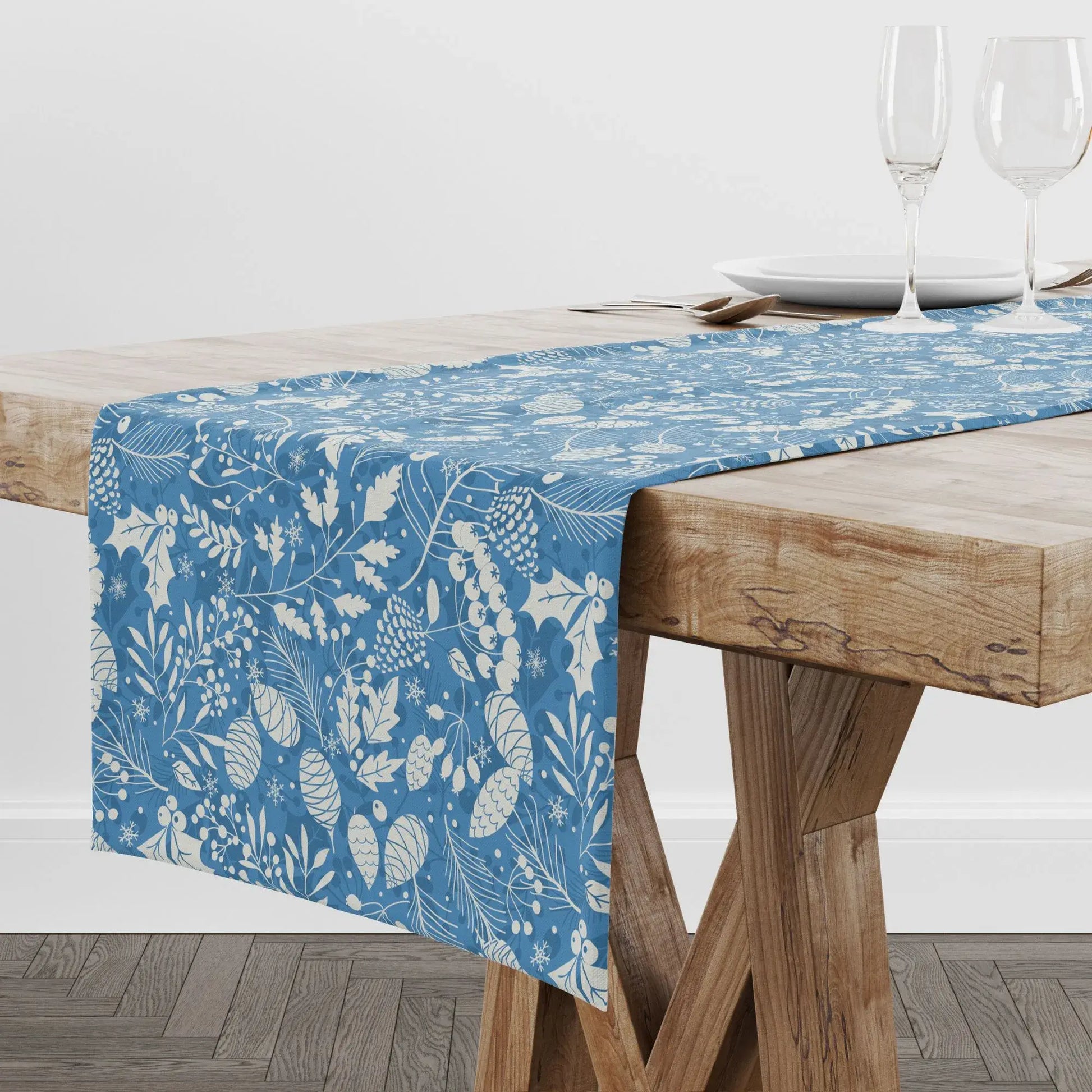 Blue Winter Botanical Christmas Table Runner displayed on a wooden dining table with elegant glassware.