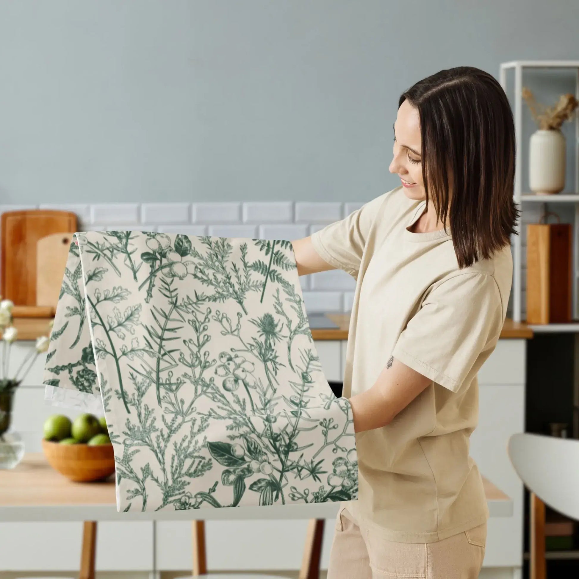 A woman holding the Botanical Christmas table runner featuring soft winter greenery in a cozy kitchen setting.