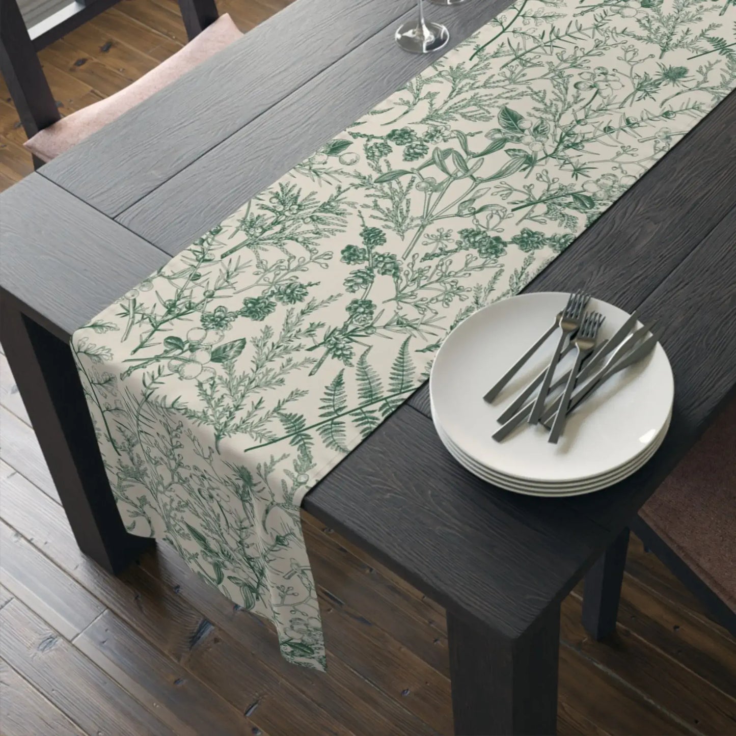Botanical Christmas table runner draped on a rustic wooden table with plates and cutlery for winter holiday decor.