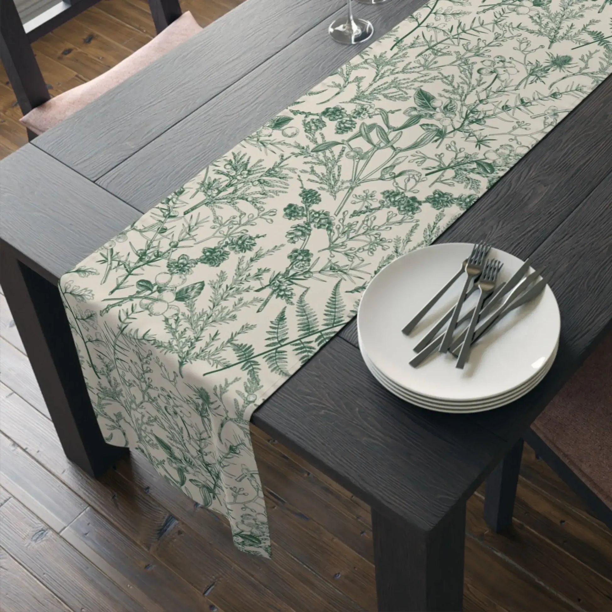 Botanical Christmas table runner draped on a rustic wooden table with plates and cutlery for winter holiday decor.