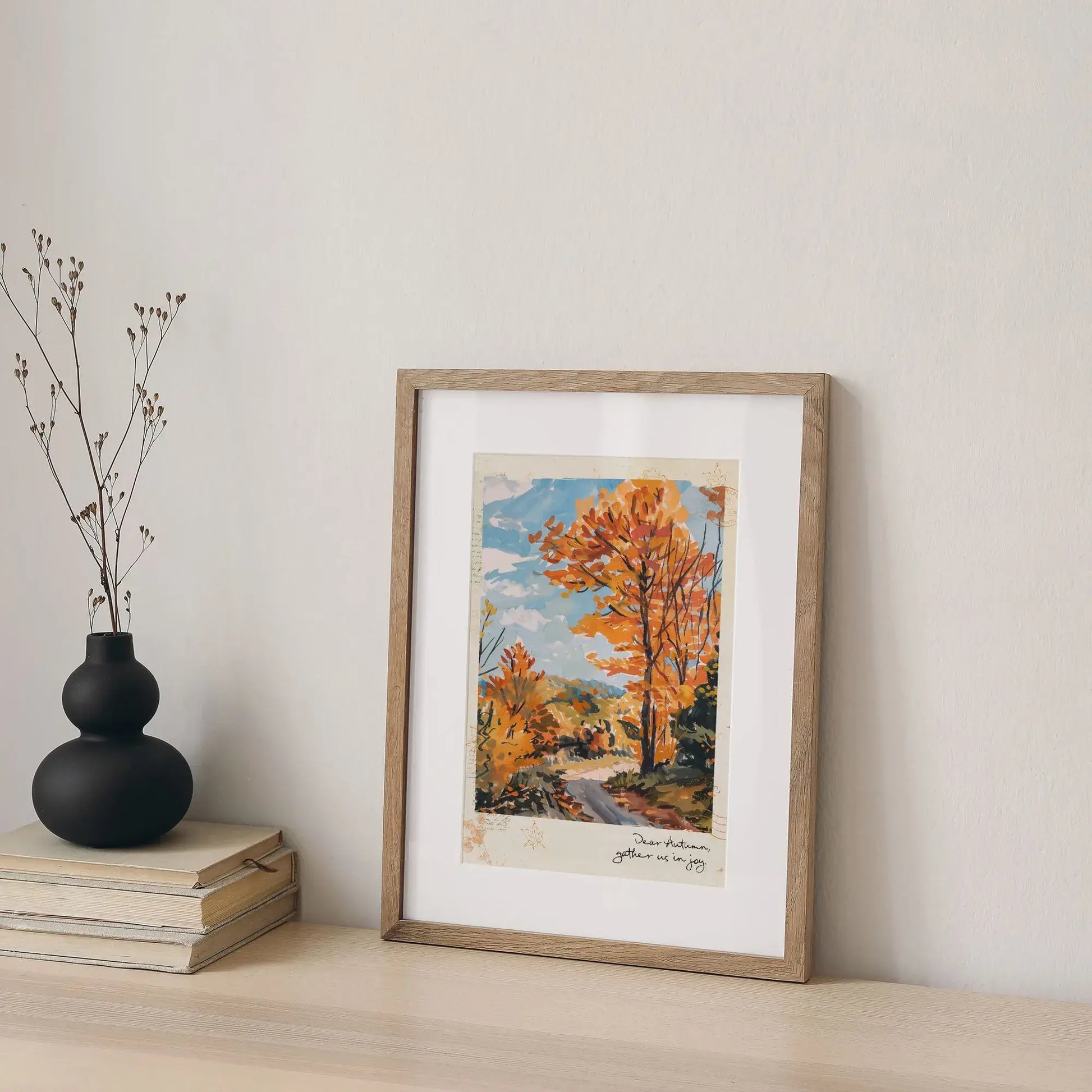 Framed autumnal wall art “Autumn Road” print with golden trees, styled on shelf with stacked books and black vase decor