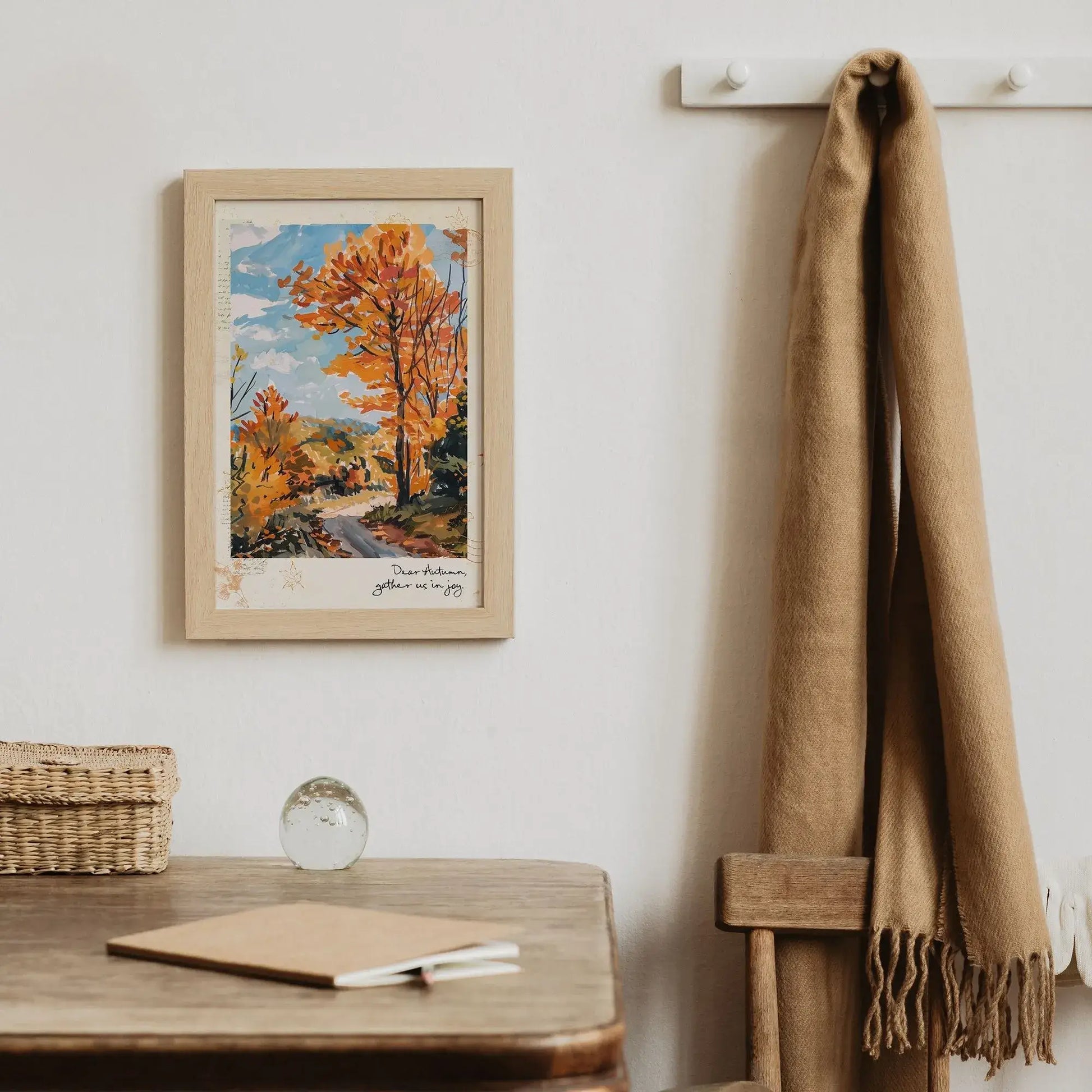 Framed autumnal wall art print “Autumn Road” with golden trees and path, styled on wall above wooden desk with basket and scarf