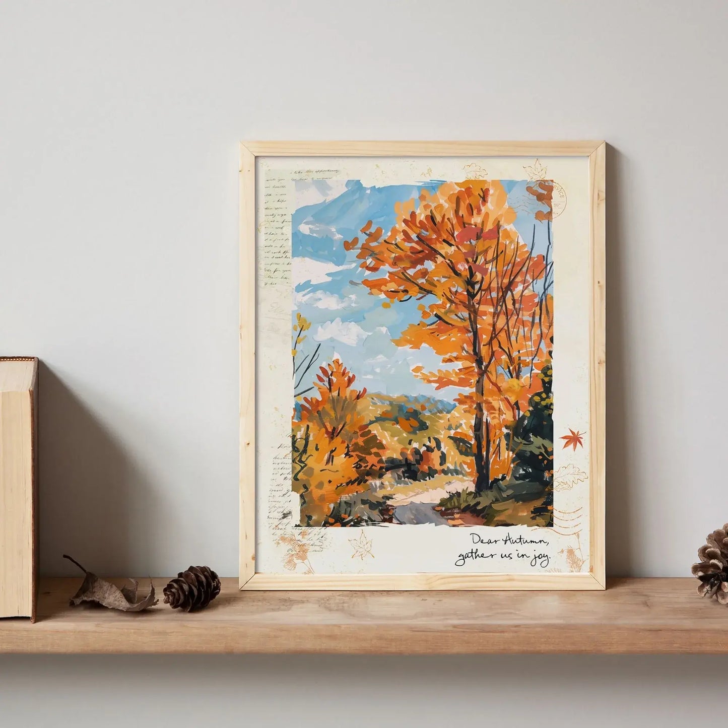 Framed autumnal wall art “Autumn Road” with golden trees and path, styled on wooden shelf with books, pinecone, and autumn leaves