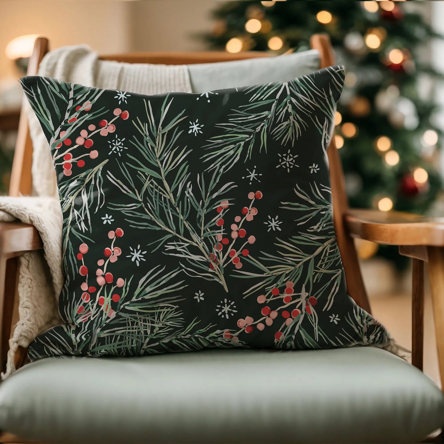 Black Christmas pillow with pine and red berry design on chair by holiday tree