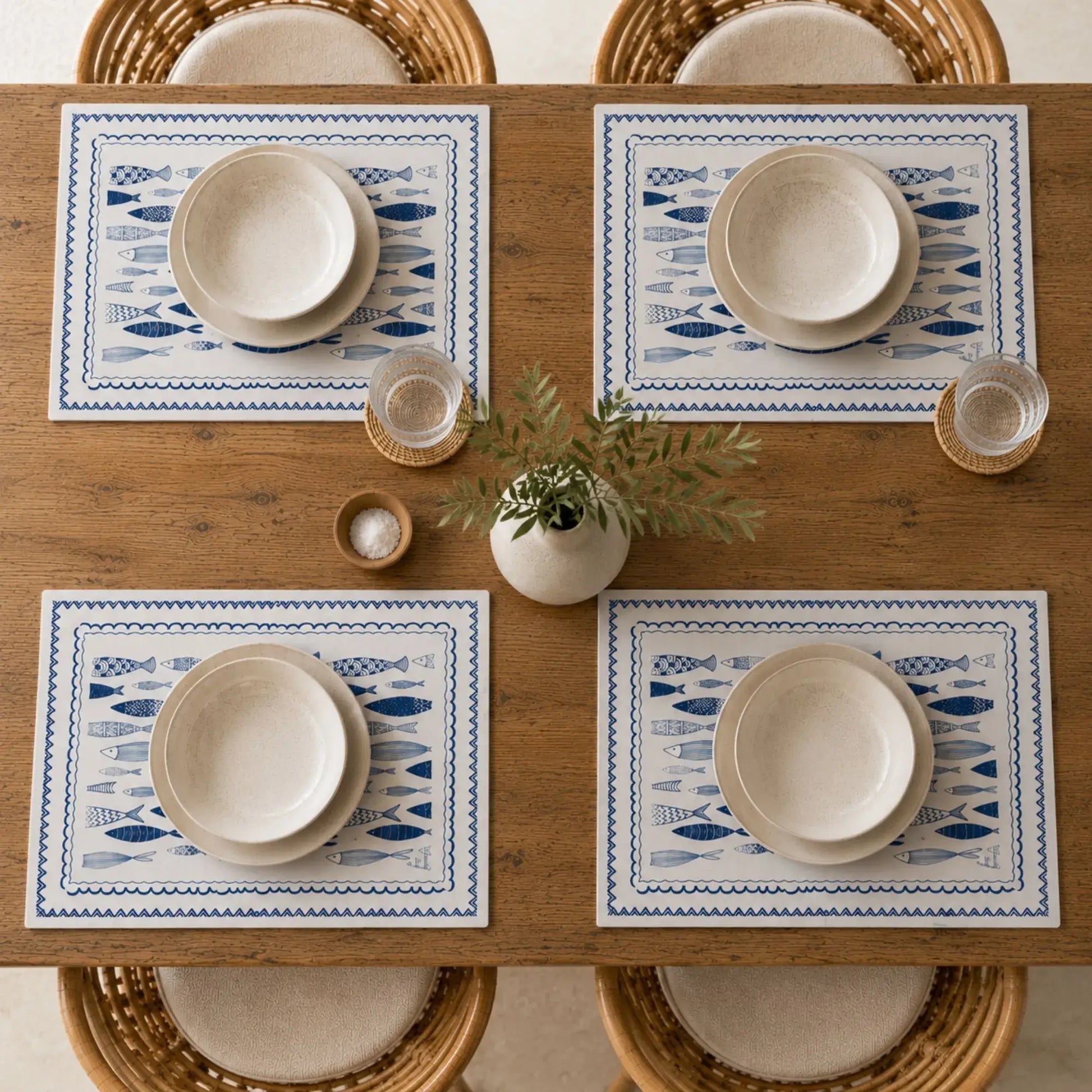 Blue Fish Cotton Placemats displayed on a wooden table with bowls and a decorative plant for a coastal dining experience.