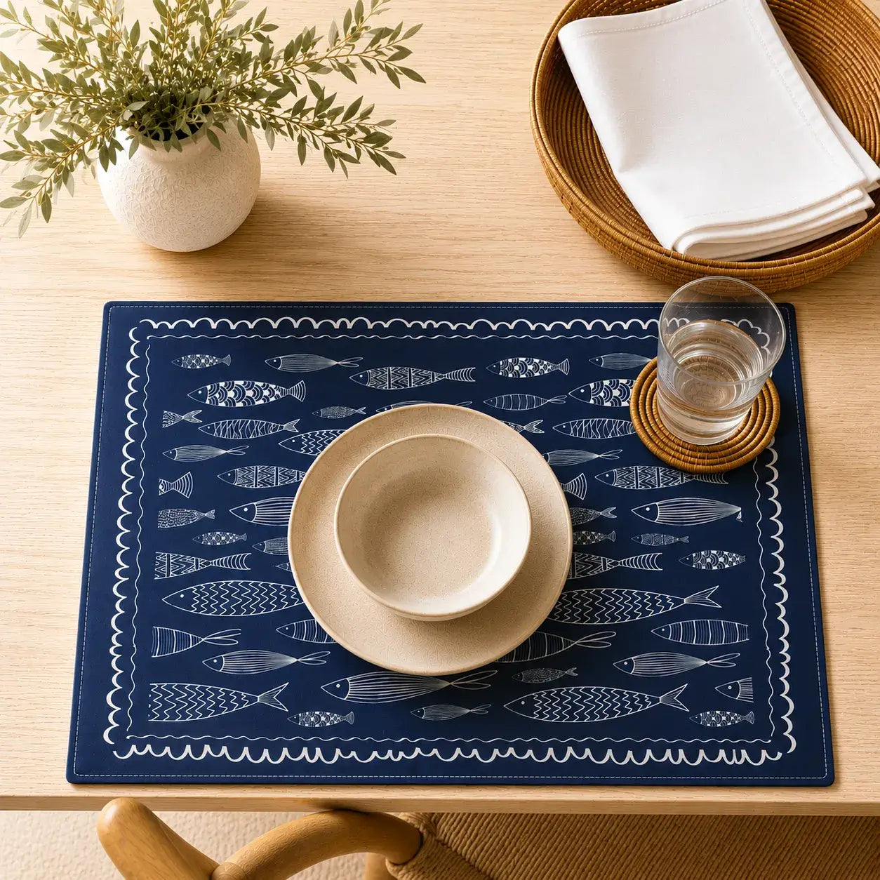 Blue Fish Cotton Placemats on wooden table with bowl, glass, and napkins, showcasing nautical fish patterns.
