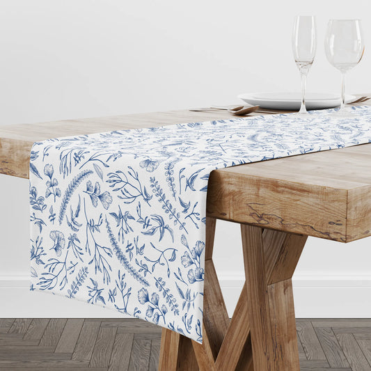 Blue Herb Botanical Table Runner displayed on a wooden table, featuring blue herb patterns and leafy stems.