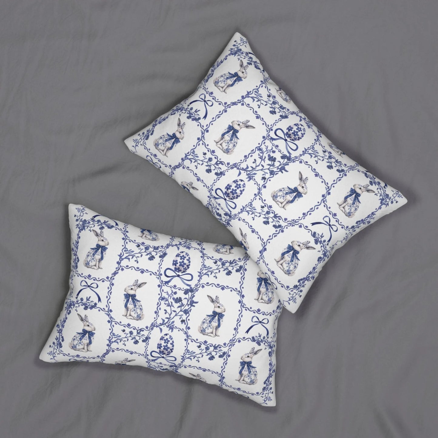 Two white lumbar pillows with a blue watercolor Chinoiserie tile pattern of rabbits and Easter eggs on a gray background.