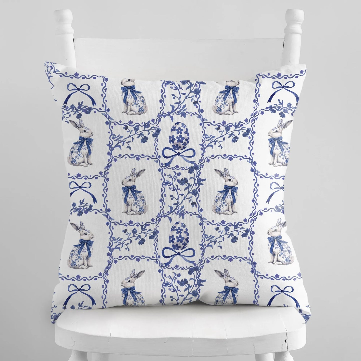 White pillow with a blue watercolor Chinoiserie pattern of rabbits, Easter eggs, and floral tiles.
