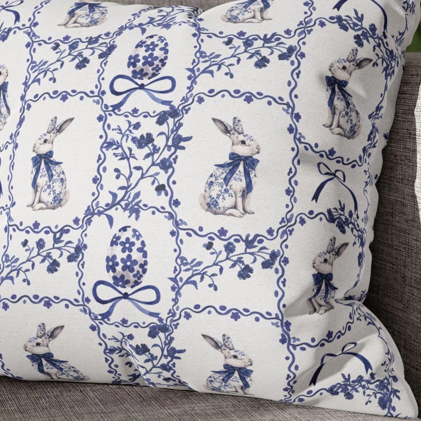 Close-up of a white pillow with a blue watercolor Chinoiserie tile design featuring rabbits with bows and decorated Easter eggs.