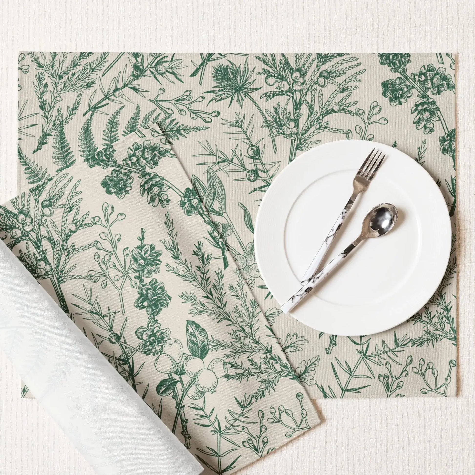 Botanical Christmas placemats featuring winter greenery and floral designs complementing a white plate and cutlery.
