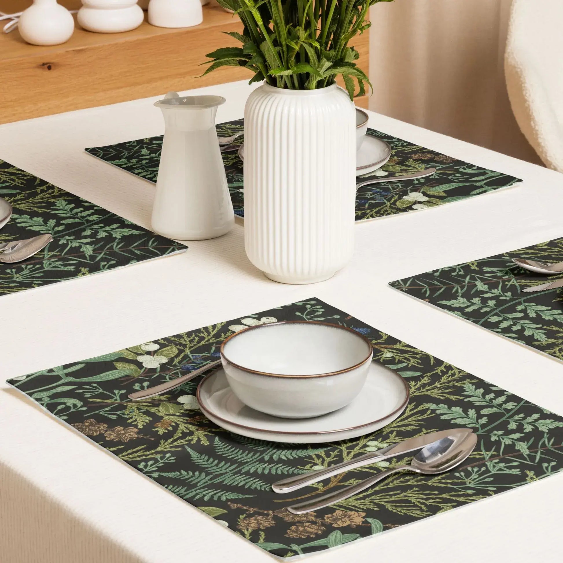 Botanical Christmas placemats on a dining table with neutral dinnerware and a plant centerpiece.
