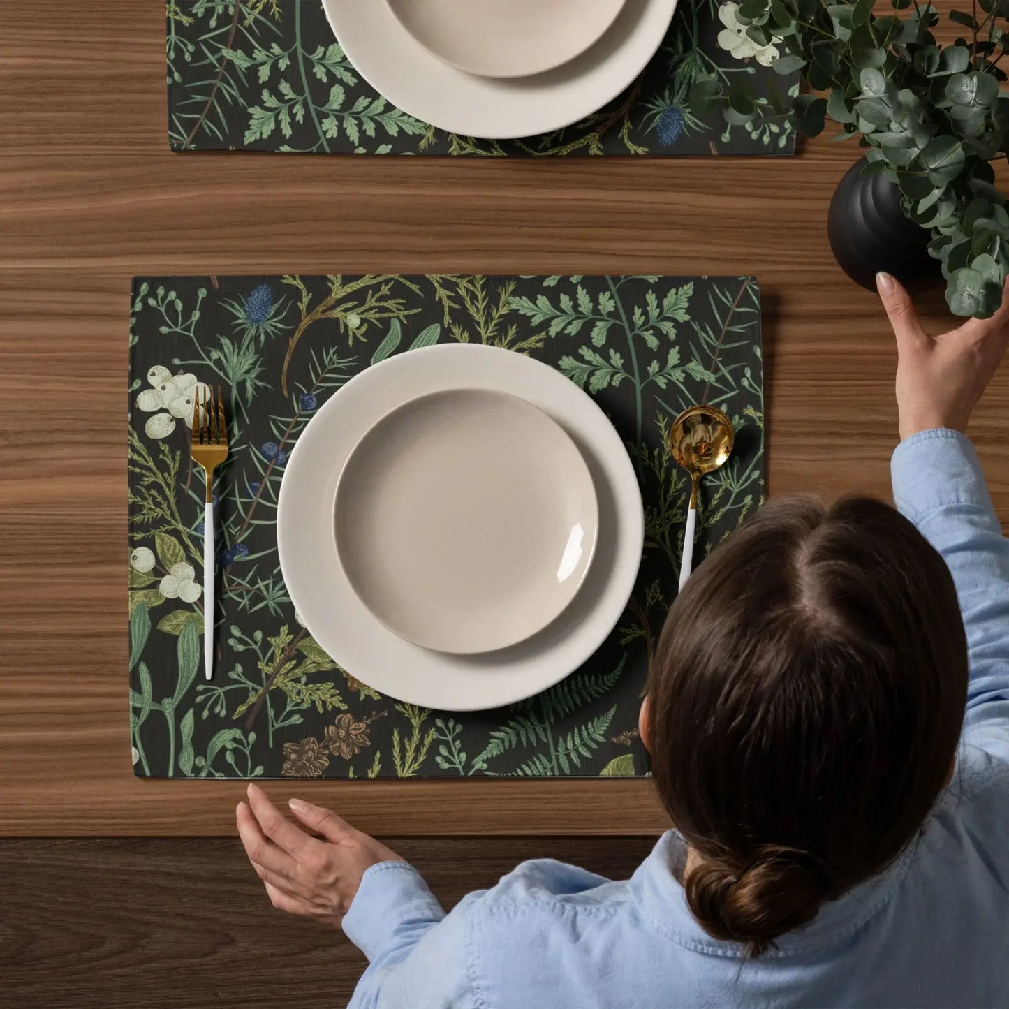 Botanical Christmas placemats set on a wooden table with neutral dinnerware and greenery for winter holiday decor.