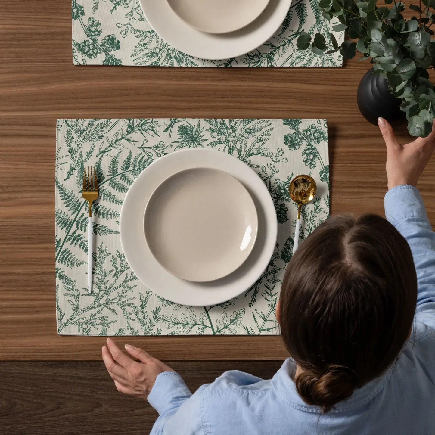 Botanical Christmas placemats set on a wooden table with plates and utensils, showcasing winter greenery decor.