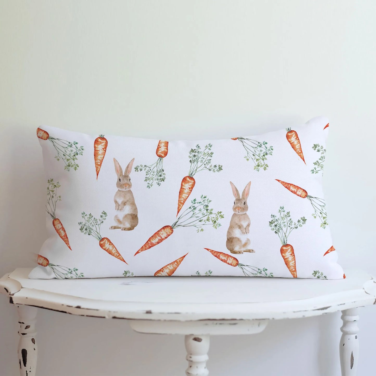 Lumbar pillow with a watercolor bunny and carrot pattern displayed on a white table, ideal for spring decor.
