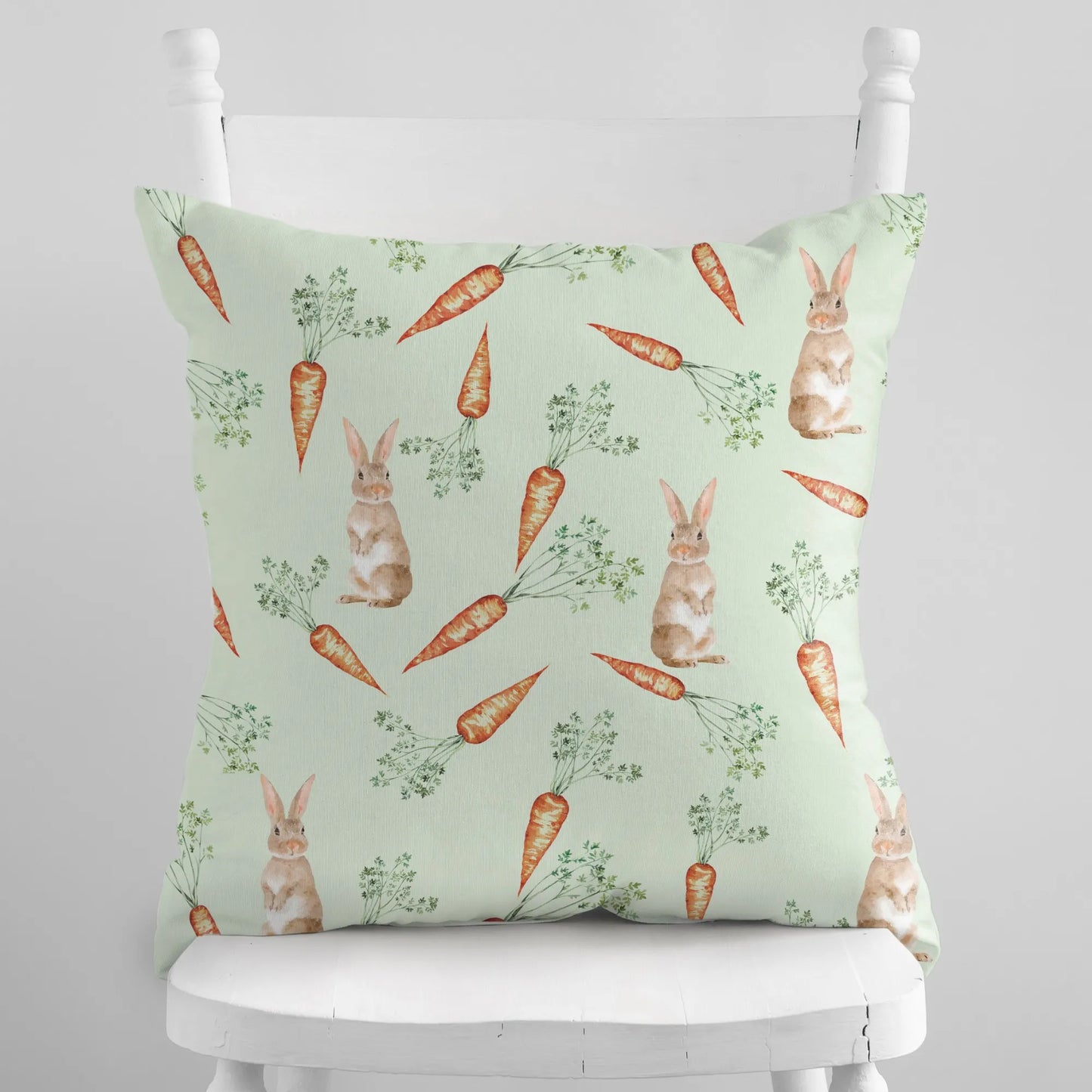 Light green throw pillow with a watercolor design of bunnies and carrots, perfect for a subtle spring touch.
