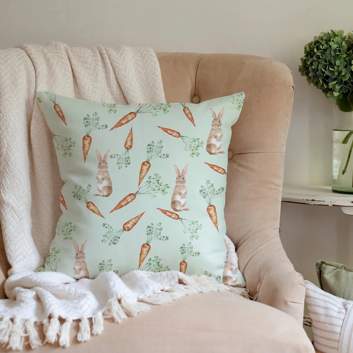 Light green watercolor bunny and carrot pillow on an armchair with a cozy throw, suggesting spring home decor.