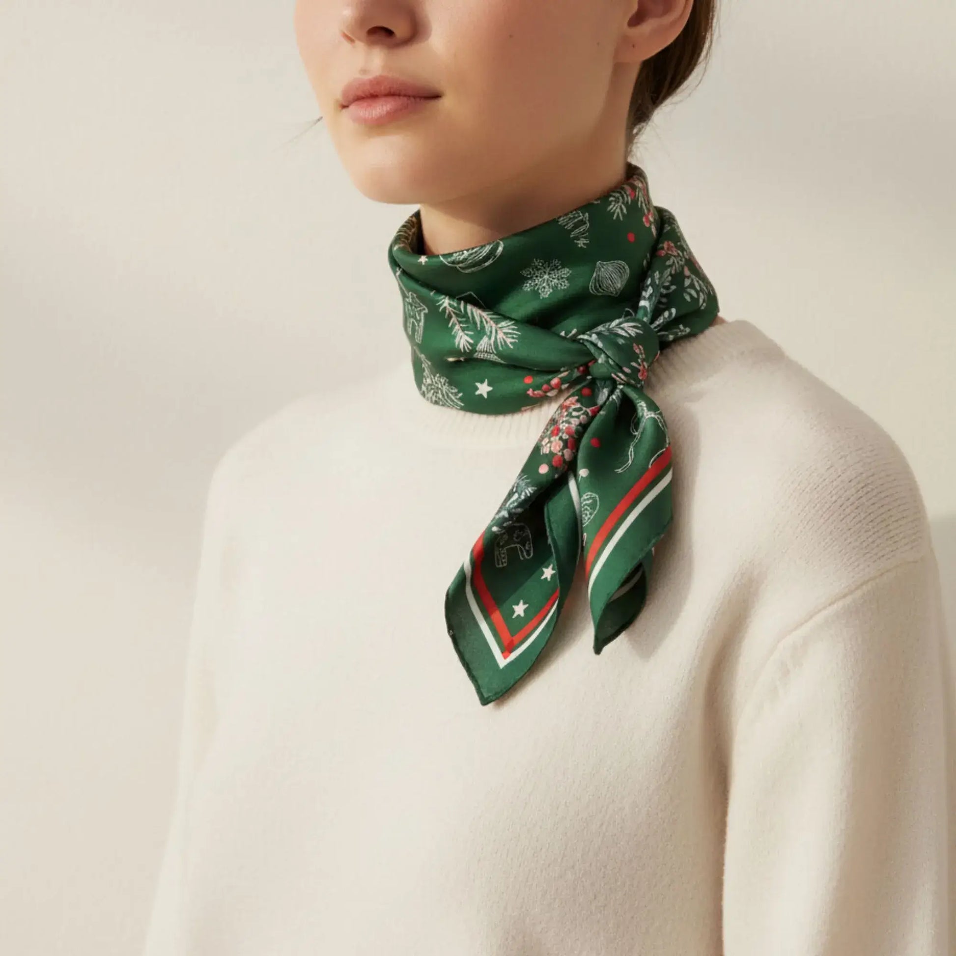 Christmas botanical silk scarf styled as a neck accessory featuring pine and red berry print on a deep green background.