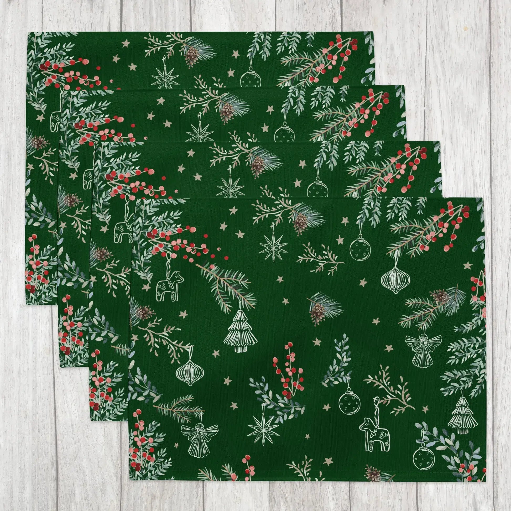 Set of green Botanical Christmas Placemats with pine and red berry design on wooden surface.