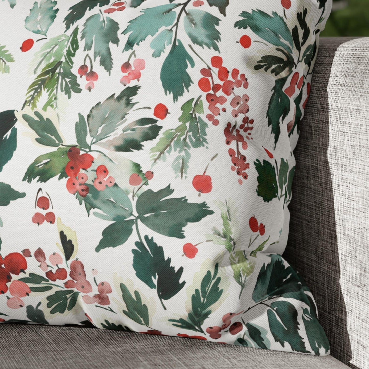 Close-up of watercolor Christmas pillow with holly berries and leaves on gray couch – festive botanical decor