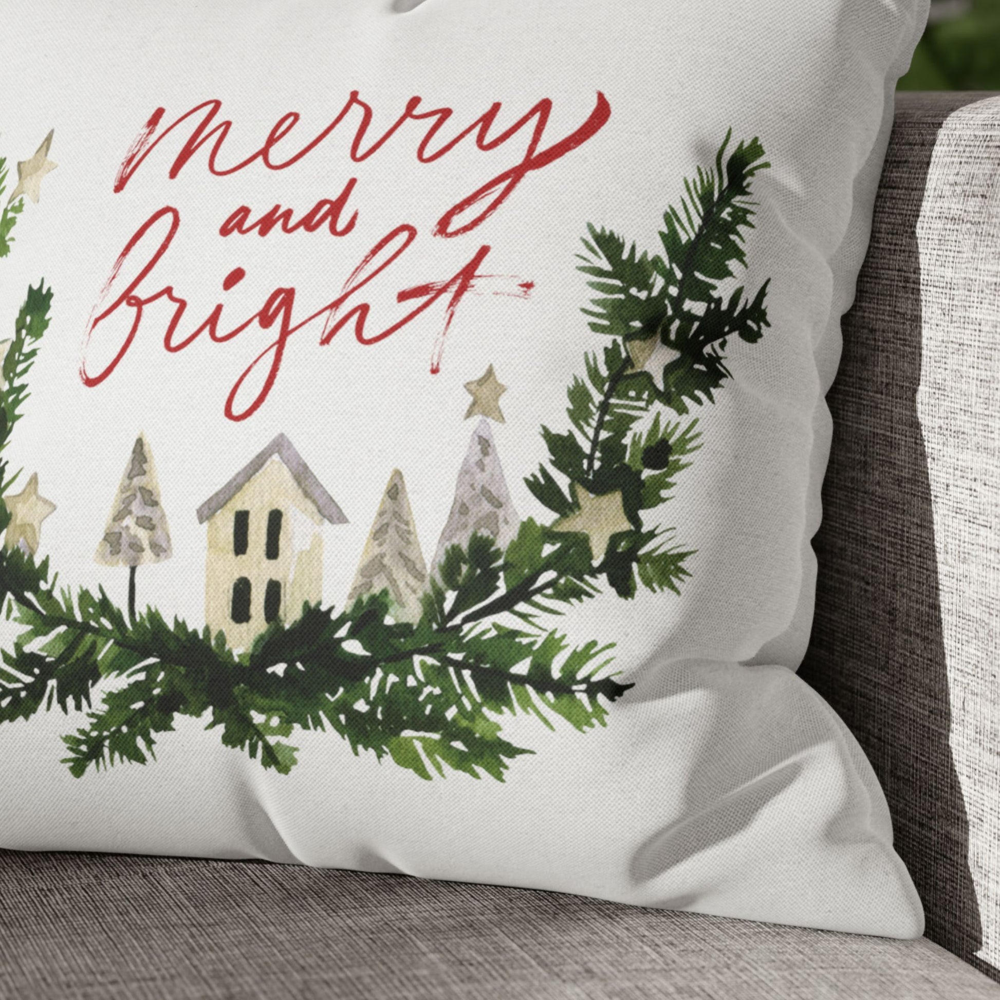 Close-up of Merry and Bright Christmas pillow with watercolor winter village and greenery on fabric texture