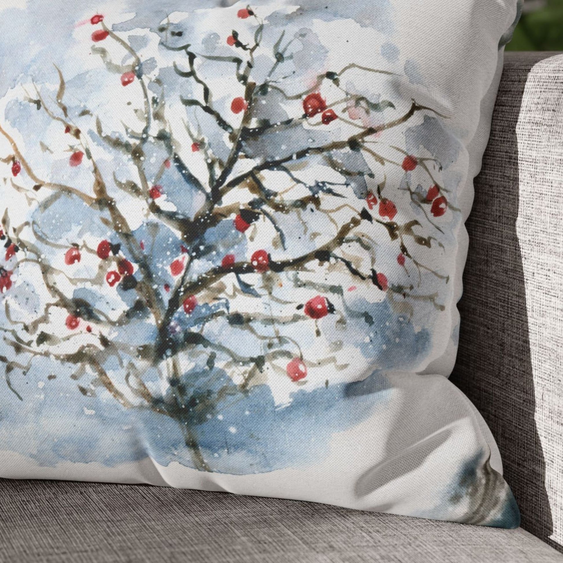 Close-up of watercolor winter pillow with red berries on snowy tree – textured fabric on neutral couch