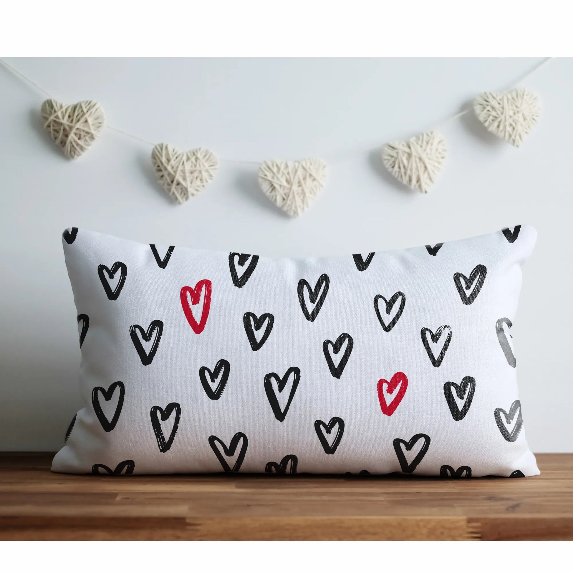 Cute Hand-Drawn Hearts Valentine Pillow by Blue Water Songs on a wooden surface. Black hearts with red accents and heart garland backdrop.