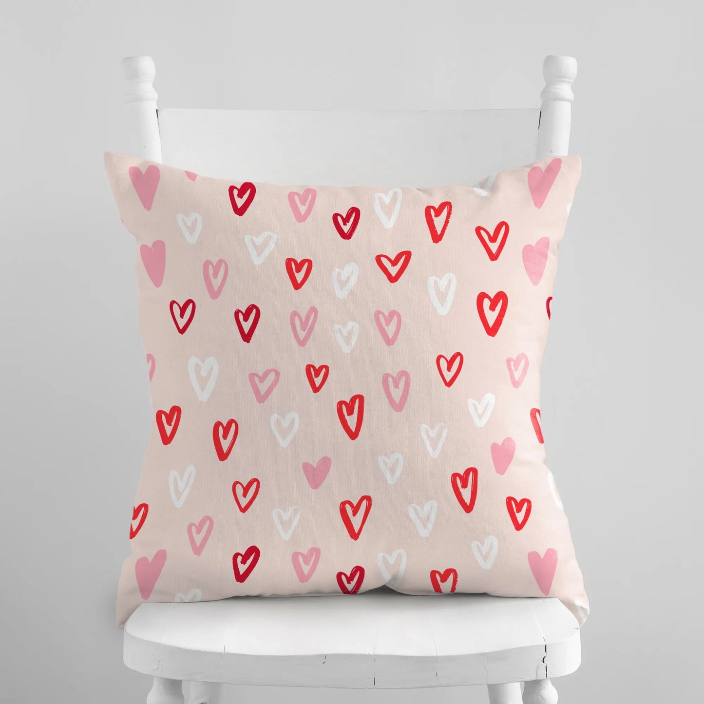 Cute hand-drawn hearts valentine pillow on a white chair, colorful heart patterns to enhance seasonal decor.
