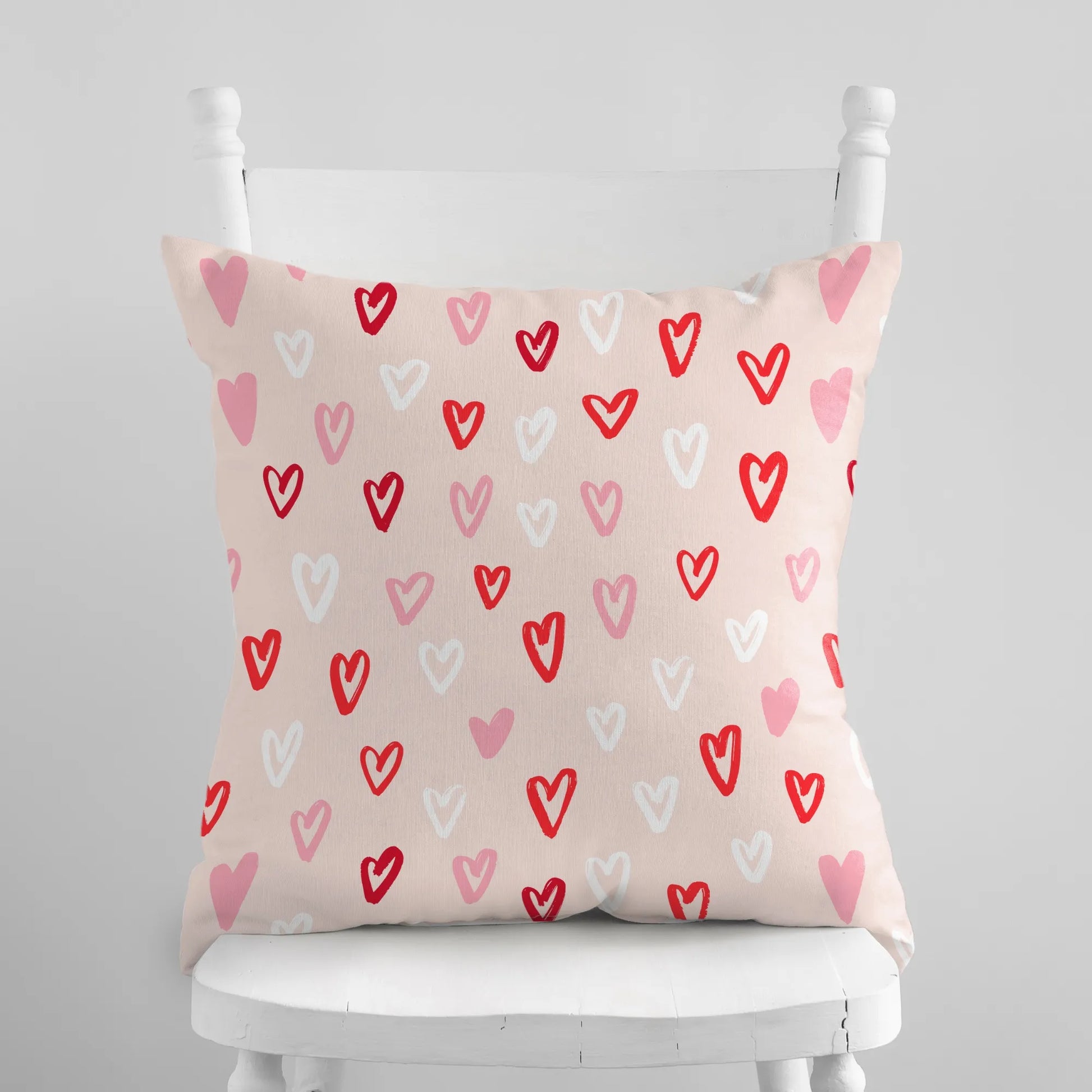Cute hand-drawn hearts valentine pillow on a white chair, colorful heart patterns to enhance seasonal decor.