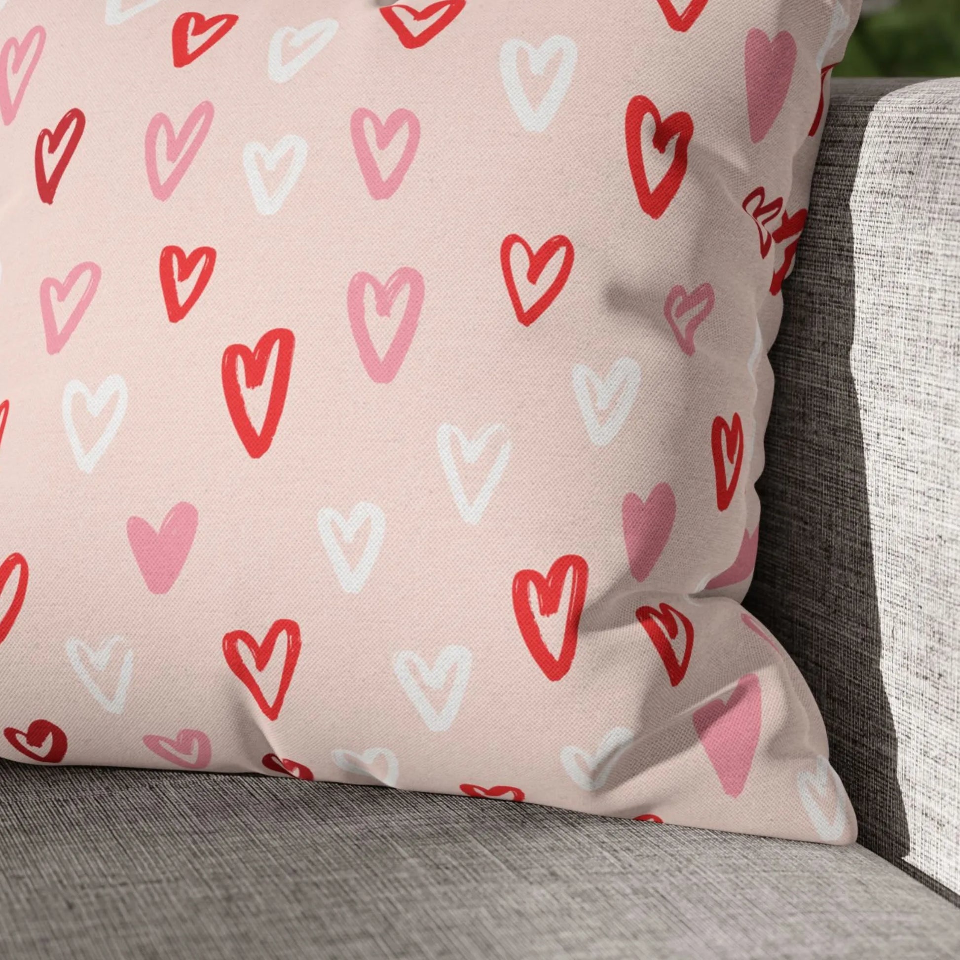 Close-up of a Cute Hand-Drawn Hearts Valentine Pillow on a gray textured couch, Blue Water Songs brand. Red, pink, and white hearts.
