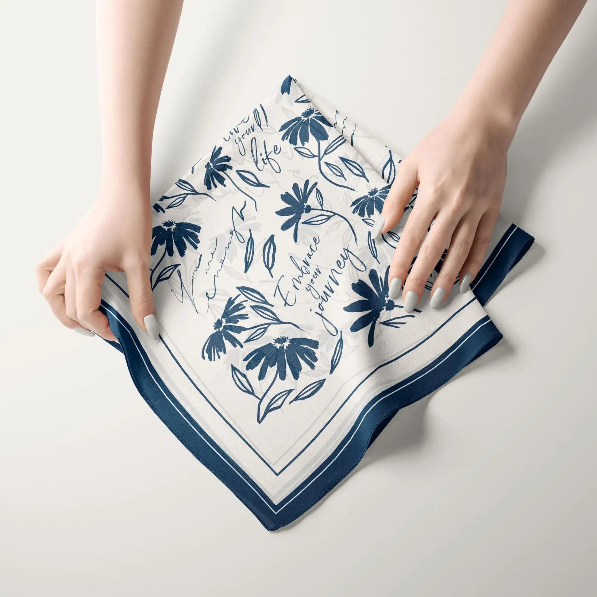Hands folding a daisy wildflowers silk scarf with minimal botanical floral design and navy border