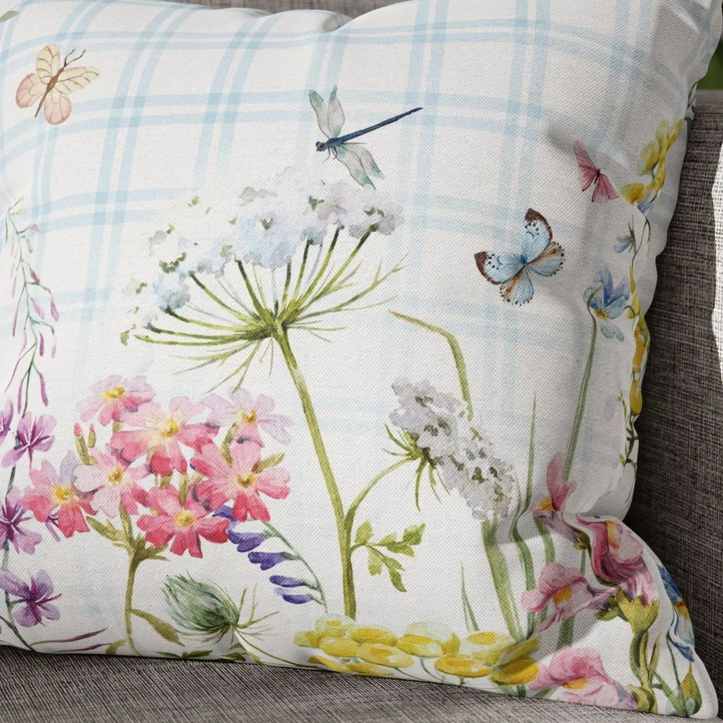 Close-up of watercolor floral throw pillow with pink, white, and yellow wildflowers and blue plaid background — nature-inspired outdoor pillow.