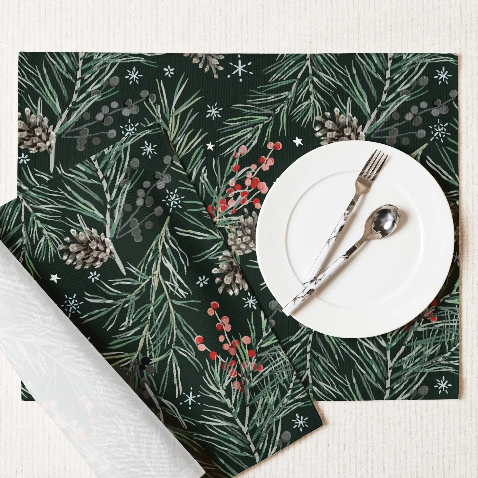 Green Pine and Berry Winter Botanical Placemats on a table with a white plate, fork, and spoon.