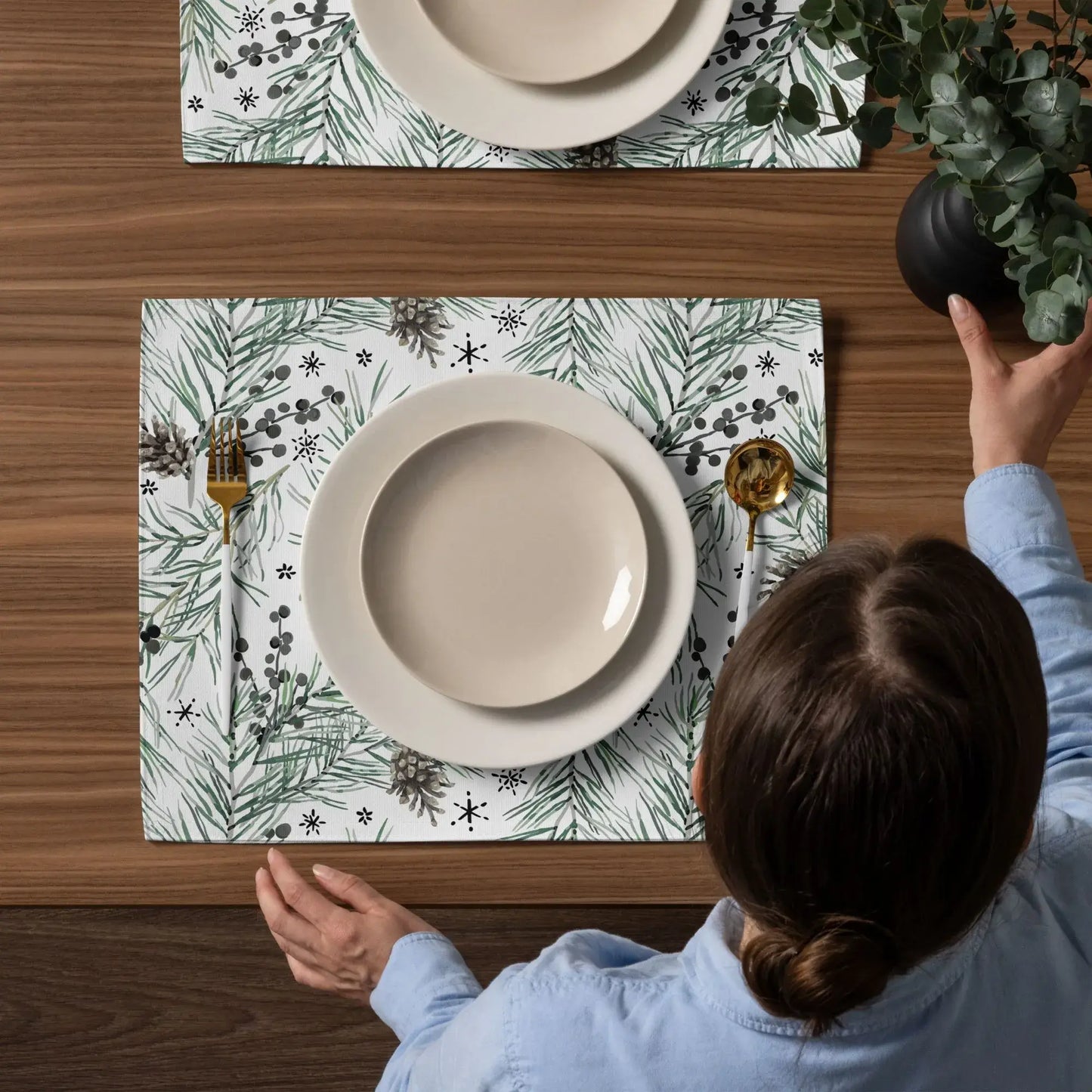 Green pine and berry winter botanical placemats on dining table with neutral dishware.
